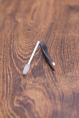 Silver tweezers for eyebrow correction and a white brush for combing eyebrows on a wooden table