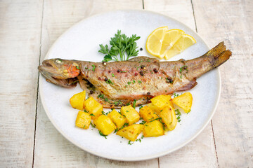 Baked trout with potato in plate. Wooden table.