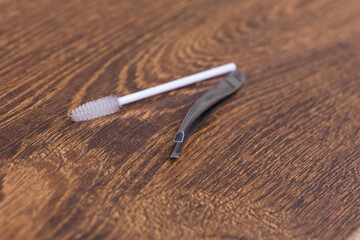 Silver tweezers for eyebrow correction and a white brush for combing eyebrows on a wooden table