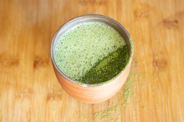 Matcha latte with matcha powder decoration served on a handmade pottery clay cup on bamboo table. Focus stacked  image from top side