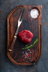 Filet mignon raw beef steak on a wooden background with seasonings and a meat fork, top view