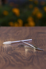 Silver tweezers for eyebrow correction and a white brush for combing eyebrows on a wooden table