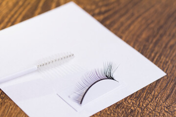 Extensions on artificial eyelashes and an eyelash brush on a white sheet