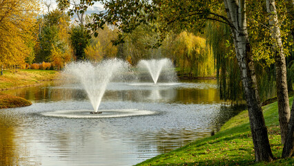 Naklejka premium Water fountains in a city park with fall colors in the trees