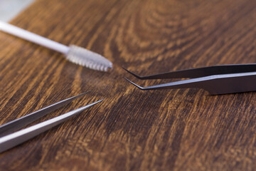 Sharp tweezers and eyelash extension brush on wooden background