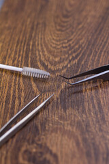 Sharp tweezers and eyelash extension brush on wooden background