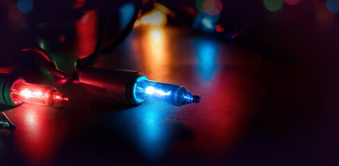 Christmas lights on dark background with bokeh lights. Xmas background texture. Small multicolored lights used for Christmas holiday trees or house decoration . Selective focus.