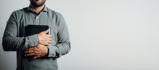 Standing man holding and hugging the bible on his chest.