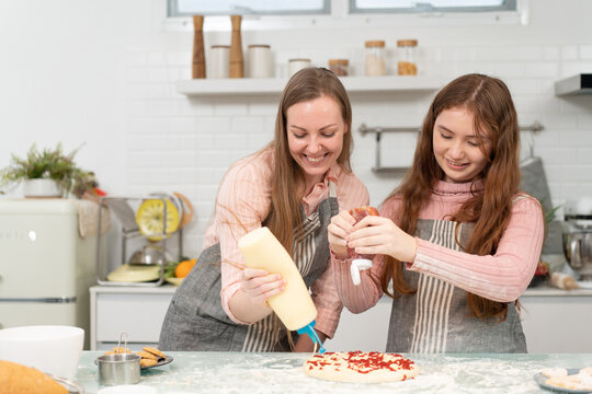 Happy mother and teen daughter enjoy decorating on pizza. woman and kid adding mayonnaise and ketchup. cooking in the kitchen at home on weekend. Family activity lifestyle