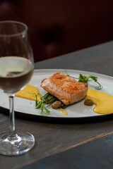 Vertical shot of a tasty seared salmon with lemon sabayon on a white plate and a glass of wine