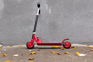The red scooter is standing next to the gray wall