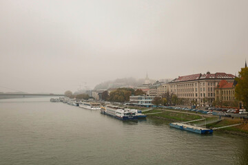 Obraz premium The foggy city of Bratislava. View of the city from the bridge. Parked ferries and ships.
