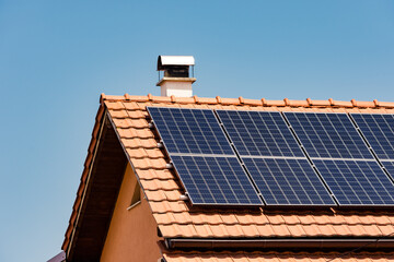 Bunch of solar panels installed on a roof of a residential home with a small chimney