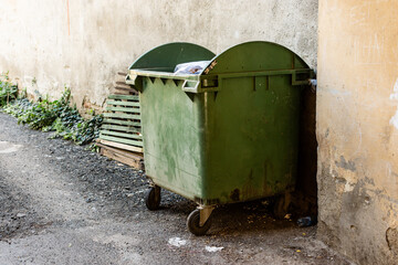 Plastic dirty dumpster next to a grunge wall of an old building in the neighborhood