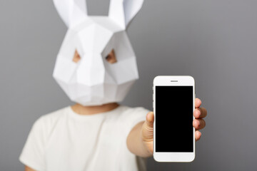 Indoor shot of anonymous woman wearing white shirt and rabbit mask posing isolated over gray...