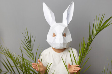 Indoor shot of unrecognizable woman wearing white shirt and rabbit mask posing isolated over gray...