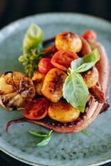 Grilled octopus tentacles with cherry tomatoes and baked baby potatoes in a blue porcelain plate on a black background. Top view, close-up.