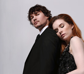 Sexy bright foxy hairstyle female woman in fashion black long skirt dress hugging with sad thinking face her serious handsome man in black suit clothing on light blue studio background. Closeup