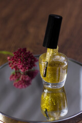 A translucent gold glitter nail polish with a rose red flower that reflects in the mirror.