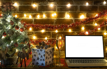Laptop with empty screen on a decorated wooden table, blur Christmas tree and gifts, light bulbs on background