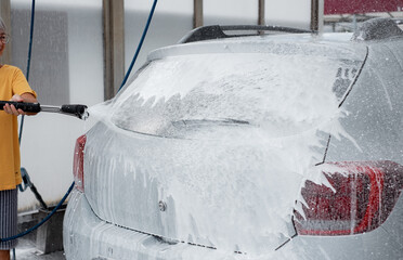 Caucasian senior woman washing her car in a self-service car wash station using high pressure...