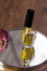 A translucent gold glitter nail polish with a rose red flower that reflects in the mirror.