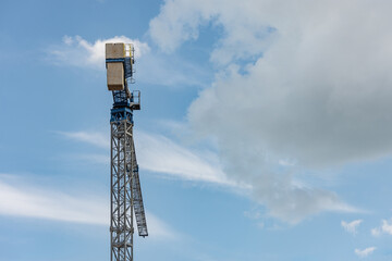 Naklejka premium High gray and blue construction crane against a cloudy sky with concrete blocks as counterweight