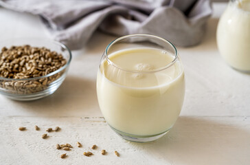Sunflower milk in glass with raw seeds, milk jar, napkin on white wooden background
