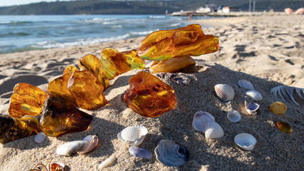 Different Baltic amber stones on a sand.  Orange and yellow amber crystals,  seashells against the...