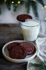 Cookies for Santa. Norwegian Christmas spiced cookies pepperkaker with glass of milk on wooden table and Christmas lights on background 