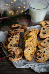 Mix of Italian homemade biskotti with different flavors (chocolate, dried fruits, pistachios ) and glass of milk on wooden table.