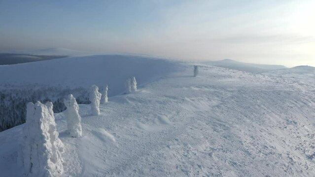 Landscape in sub-zero temperatures from above. Clip.Snowy empty mountains with frozen hills and trees are visible against a bright sky.
