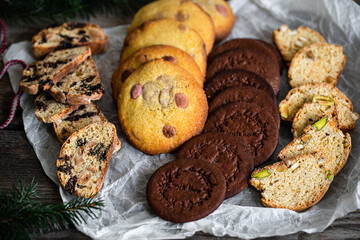 Mix of different kinds of Christmas cookies: biscotti, American chocolate cookies and nordic spicy gingerbread cookies  on baking paper on wooden table.