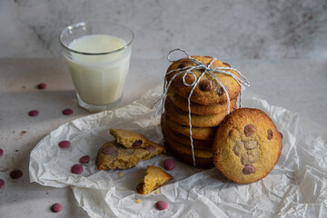 Stack of homemade American cookies with raspberry chocolate morsels and glass of milk on white background.