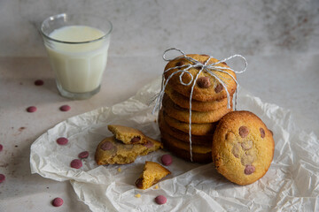 Stack of homemade American cookies with raspberry chocolate morsels and glass of milk on white background.
