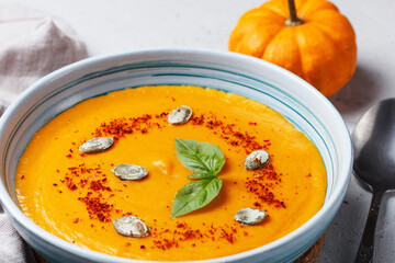 Cream soup of baked pumpkin and carrots with cream and pumpkin seeds with herbs on a gray background. Vegan food.Close up