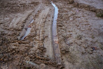 Obraz premium Braune Schlammlandschaft mit Fahrspurmuster und Wasser am Morgen im Winter 