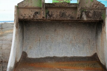 Silberne alte Baukranschaufel mit brauner nasser Bodenfläche vor blauem Pool am Morgen im Winter