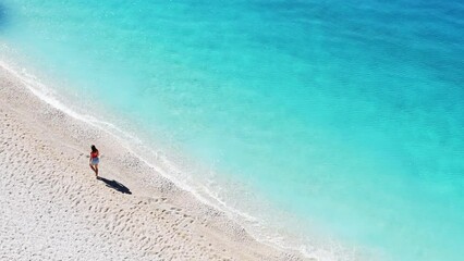 A tourist walking on a beautiful sandy beach with gentle waves and crystal clear water.