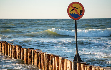 Wooden breakwaters. Sign forbidding jumping from breakwaters into the sea. Beach hazard warning...