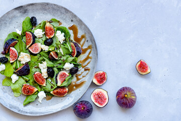 Top view of fresh healthy summer salad with figs, white cheese, arugula and black olives seasoned with sauce on grey ceramic plate on grey background. Close-up. Flat lay composition. Copy space.