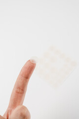 Close-up round acne patch on finger on white background. Acne patches for treatment of pimple and rosacea close-up. Facial rejuvenation cleansing cosmetology.