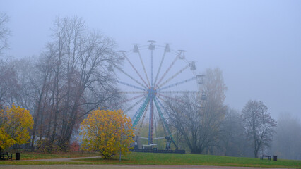 Ferris wheel in an old abandoned park in autumn in thick fog. There are no people in the park