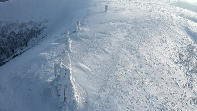 Landscape in sub-zero temperatures from above. Clip.Snowy empty mountains with frozen hills and trees are visible against a bright sky.