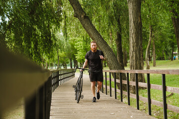 Adult handsome tattooed bearded man walking with bicycle in park