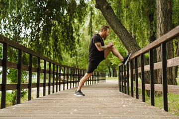 Sideview of young handsome tattooed bearded man stretching his leg