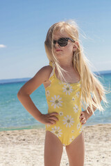 Portrait of 4 years old girl in yellow swimsuit and long blonde hair with blue sea and sky on the...
