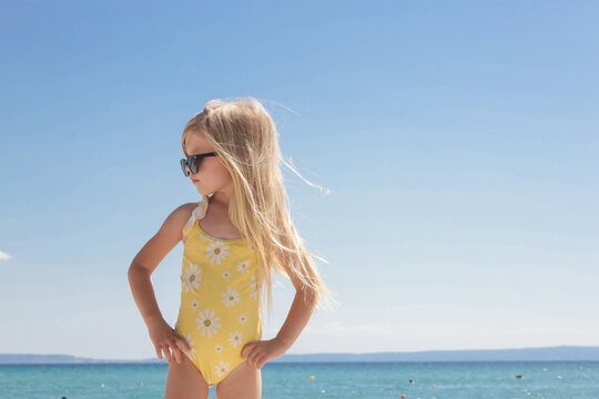 Portrait of 4 years old girl in yellow swimsuit and long blonde hair with blue sea and sky on the sandy beach	