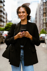Fototapeta premium Brunette young woman smiling and using mobile phone at city street