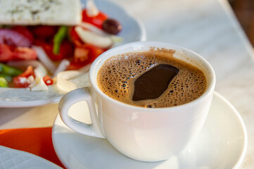 Greek coffee placed on dinning table with colourful Greek salad blurred at background